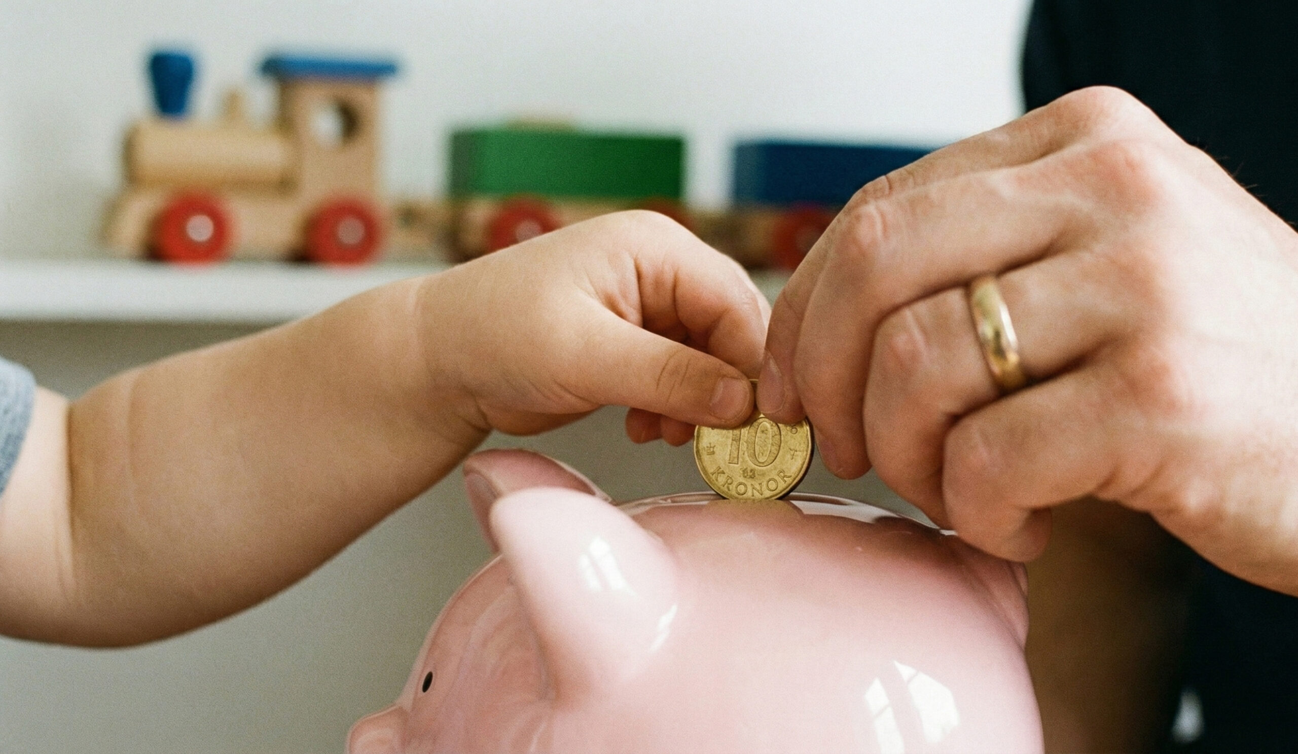 Barn och vuxen sparar tillsammans i spargris, symboliserar långsiktigt sparande till barn.
