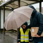 Förälder håller paraply över barn vid busshållplats som symbol för barnförsäkring